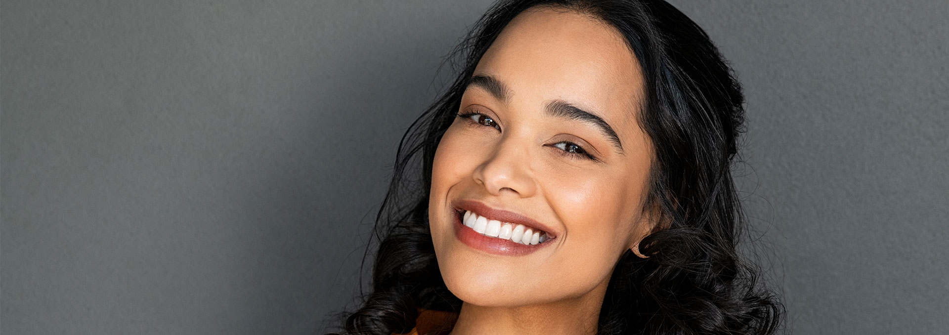 The image is a photograph of a smiling woman looking directly at the camera, with her head cropped out from the shoulders up.