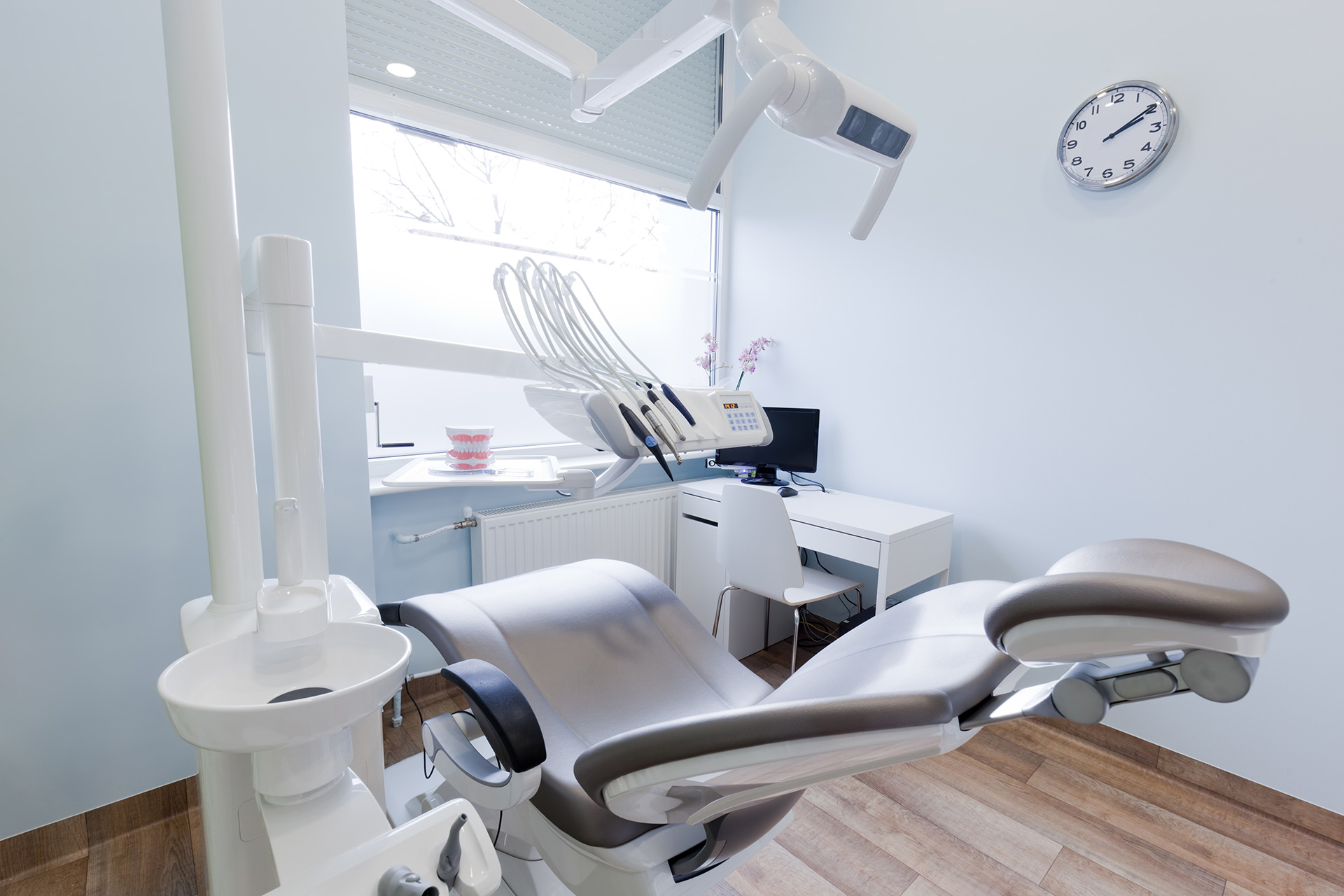 An image of a modern dental office interior with a large dental chair and equipment, set against a blue wall.