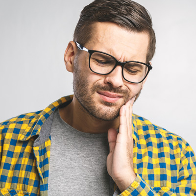 The image features a man with glasses, wearing a plaid shirt and holding his hand to his mouth, possibly in pain or discomfort.