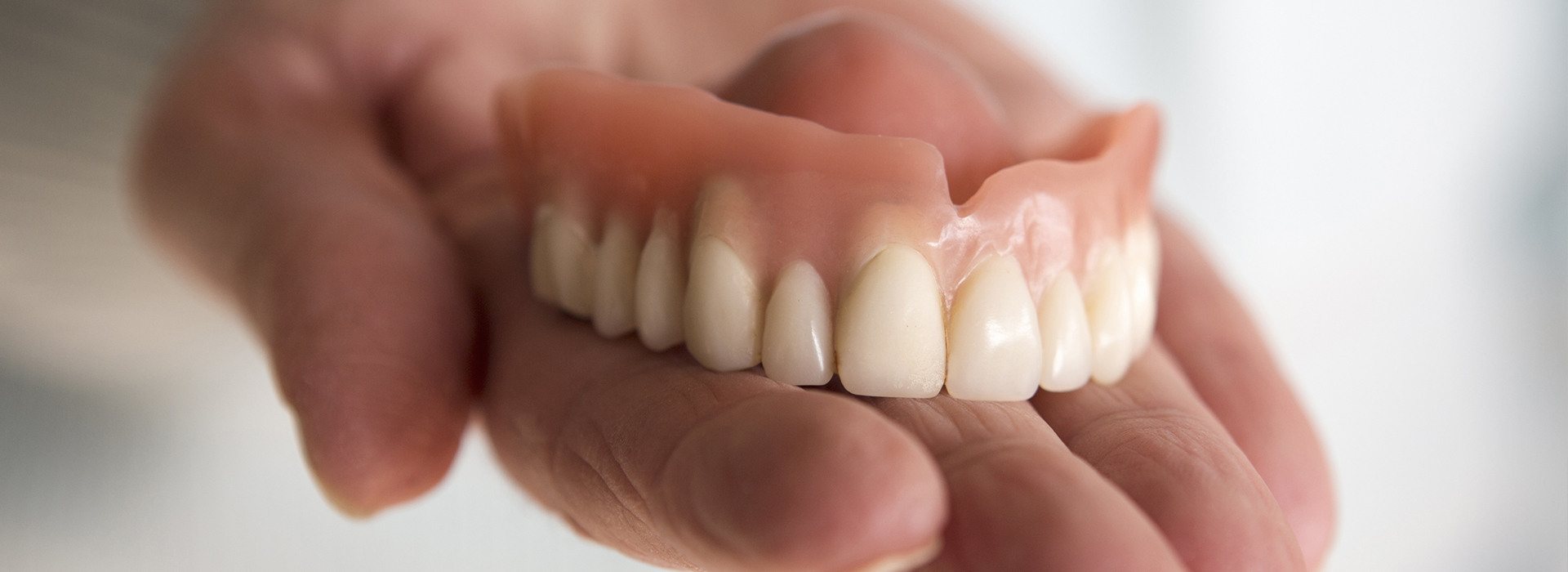 The image shows a person holding a set of dentures, which are artificial teeth, with their left hand.