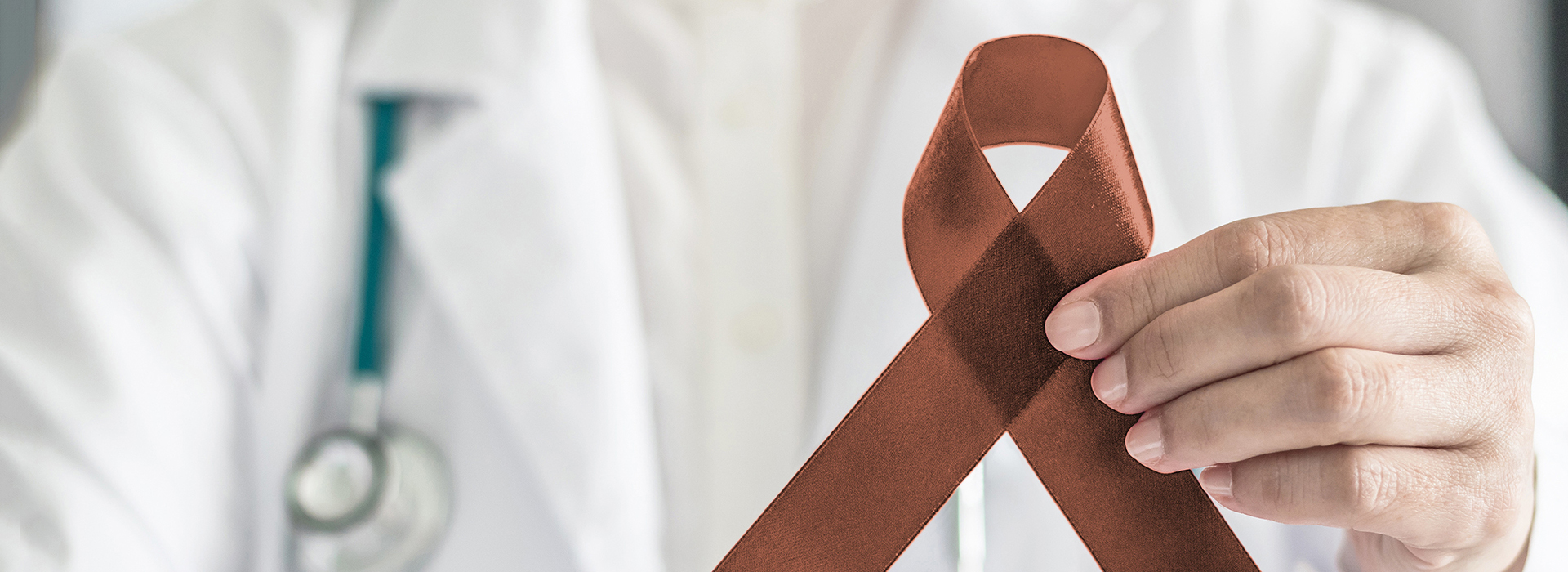 The image shows a person holding a red ribbon with a medical cross symbolizing healthcare, against the backdrop of a blurred image of a professional in a white coat, suggesting a connection to health or medical awareness.