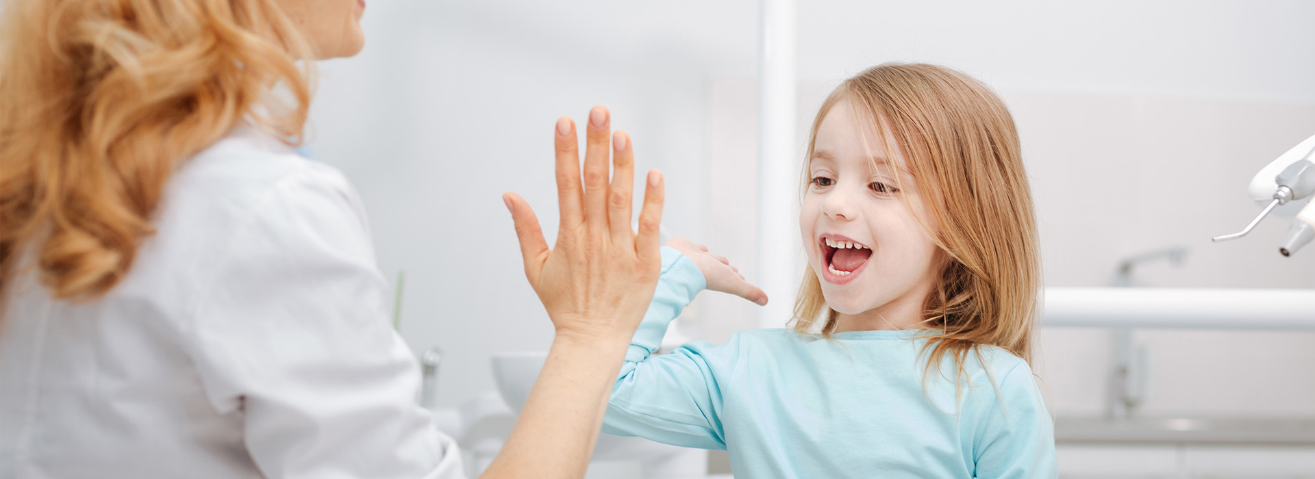 An adult and a child in a dental setting, with the adult showing their teeth to the child.