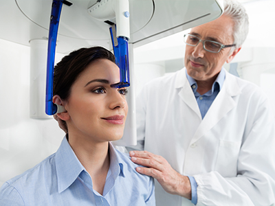 A woman is seated in a dental chair, and a man is standing behind her, both inside a modern dental office.