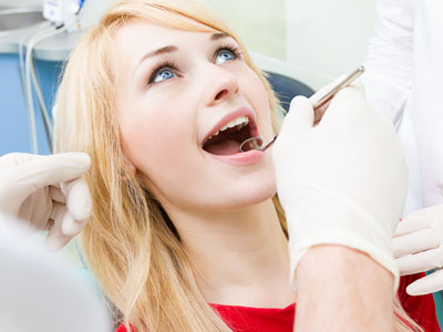 A woman is seated in a dental chair, receiving dental treatment with a smiling expression.