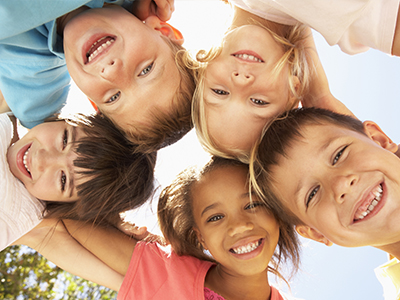 A group of children, with a mix of genders and ages, joyfully posing for a photo in the sunlight.